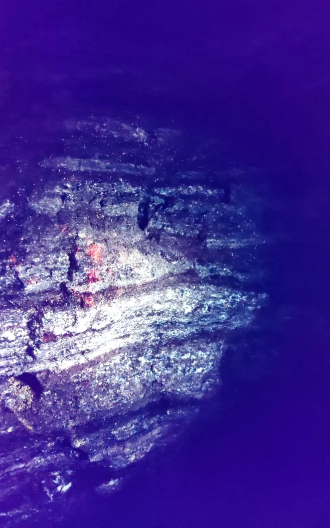 UV light on pegmatite surface showing faint orange fluorescence