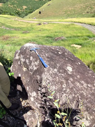 Field geologist examining a coarse-grained granite boulder with visible feldspar and quartz.