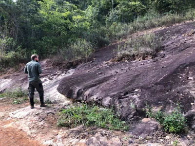 Geologist examining a foliated outcrop with dark biotite-rich bands and surface weathering.