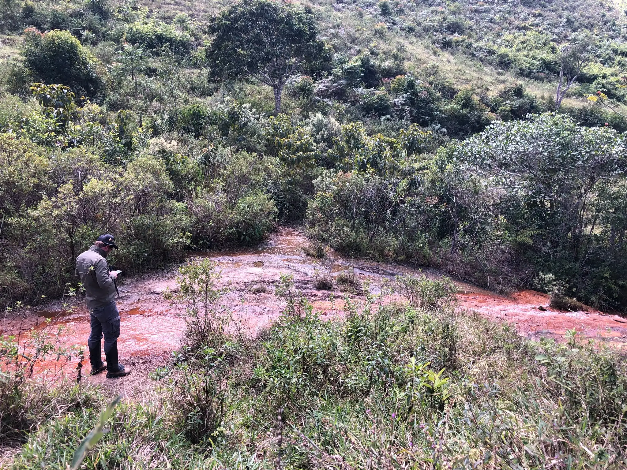 Geologist inspecting an oxidized drainage channel where surface water interacts with exposed granitic bedrock.