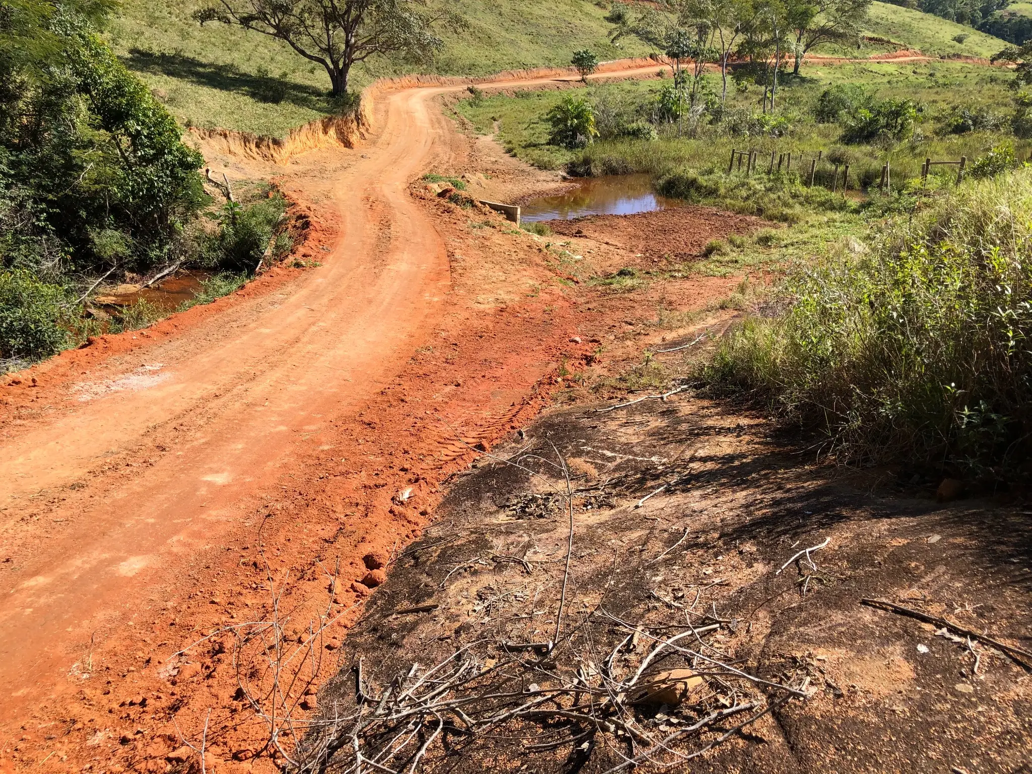 Red lateritic access road through weathered terrain with small drainage ponds nearby.