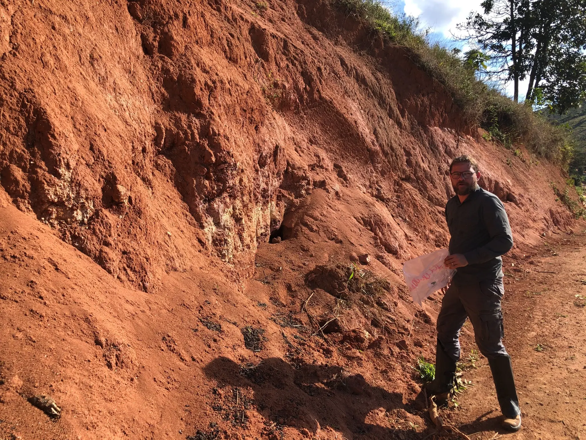 Geologist collecting samples from a red clay-rich weathered roadcut.
