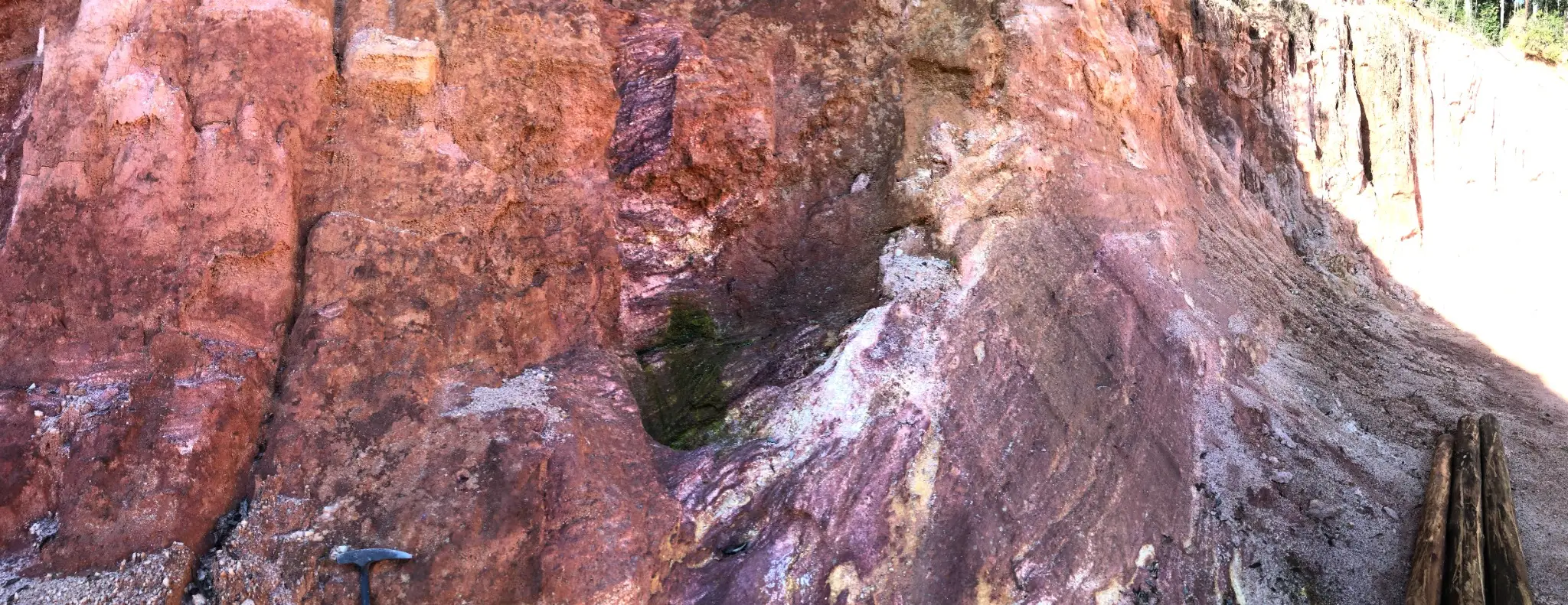 Weathered pegmatitic face with iron staining and quartz-rich zones in outcrop.