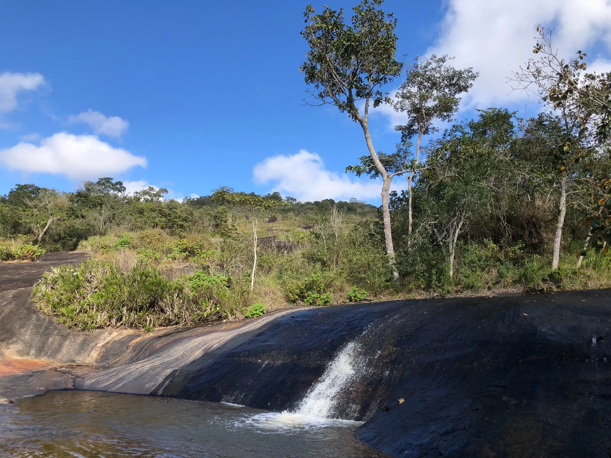 Stream cutting across exposed granite dome with small waterfall feature.