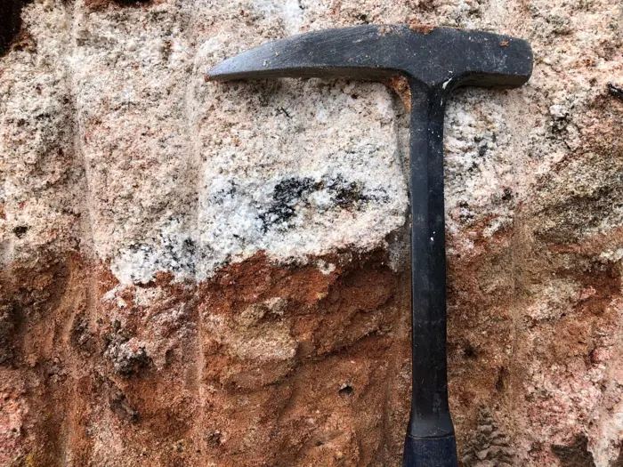 Close view highlighting dark tourmaline clusters within an iron-stained pegmatitic matrix. The red-brown kaolinized textures reflect intense tropical weathering of an originally quartz-feldspar-tourmaline assemblage — typical of lithium-fertile granitic pegmatites.