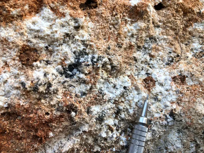 Weathered exposure showing pegmatite and schist with iron staining and tourmaline relics.