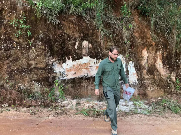 Field geologist examining oxidized pegmatite with quartz-feldspar banding